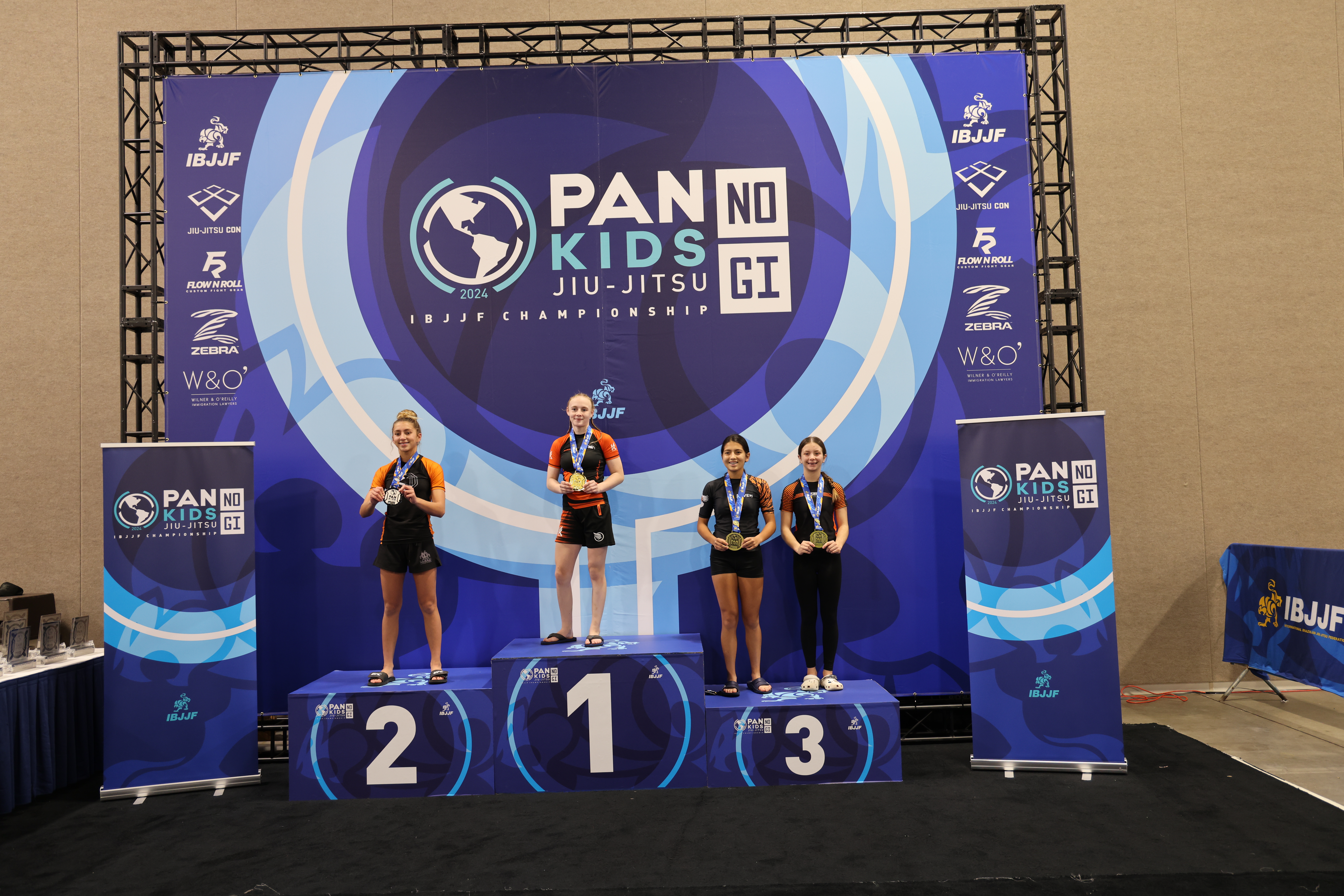 Fotografía del podio del Pan Kids IBJJF No-Gi Championship 2024. El escalón más alto del podio lo ocupa la campeona de la división. La identidad gráfica del evento es visible en el fondo: PAN KIDS NO-GI IBJJF CHAMPIONSHIP.